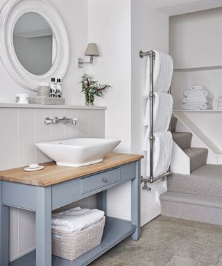 Bathroom with white hand basin on a grey table, tiled floor and towel rail with white towels.