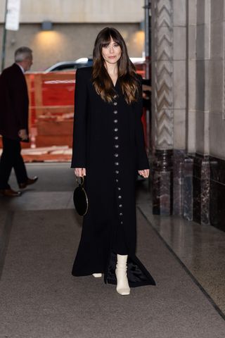 Elizabeth Olsen wears a handbag by The Row in March 2025 along with a black coat and white boots