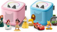 A pink Toniebox 2 with Merida, Ariel, Moana, and Belle. It's next to a blue Toniebox 2 with Simba, Lightning McQueen, Winnie The Pooh, and Baloo. 