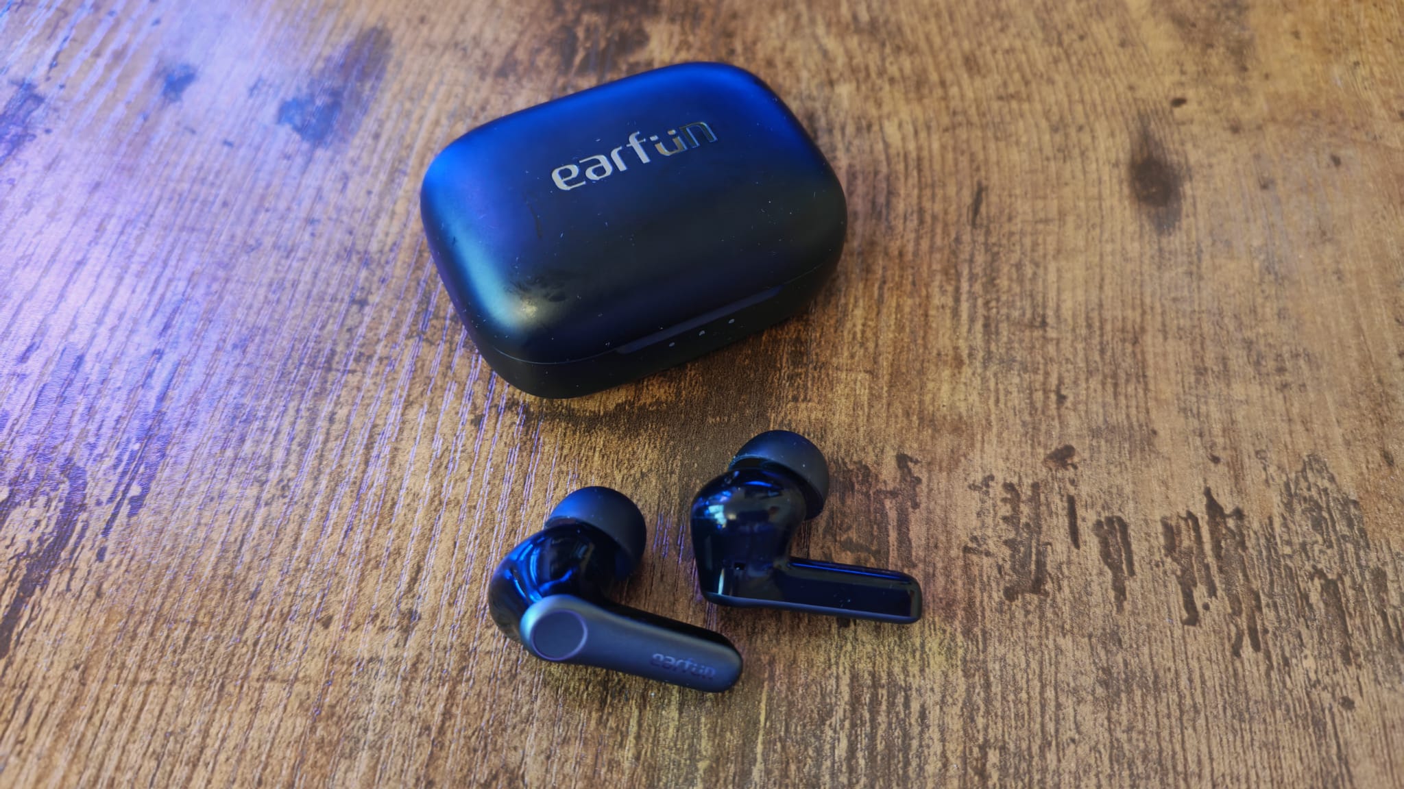 The EarFun Air Pro 4 earbuds lying on a desk next to their charging case