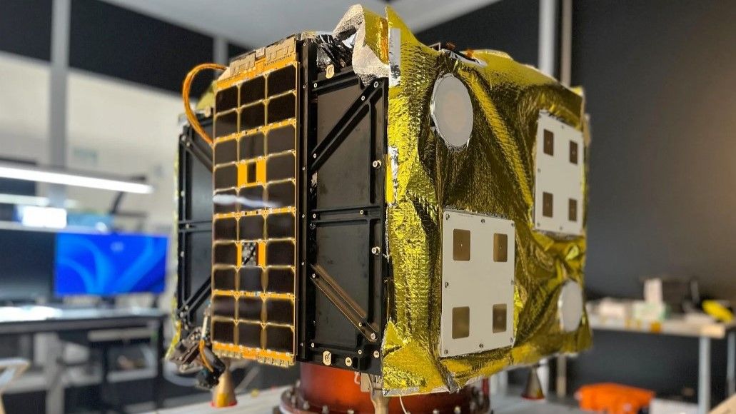 A cube shaped spacecraft sits secured to a metal table.