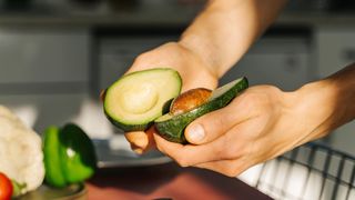 Woman's hands holding half cut avocado