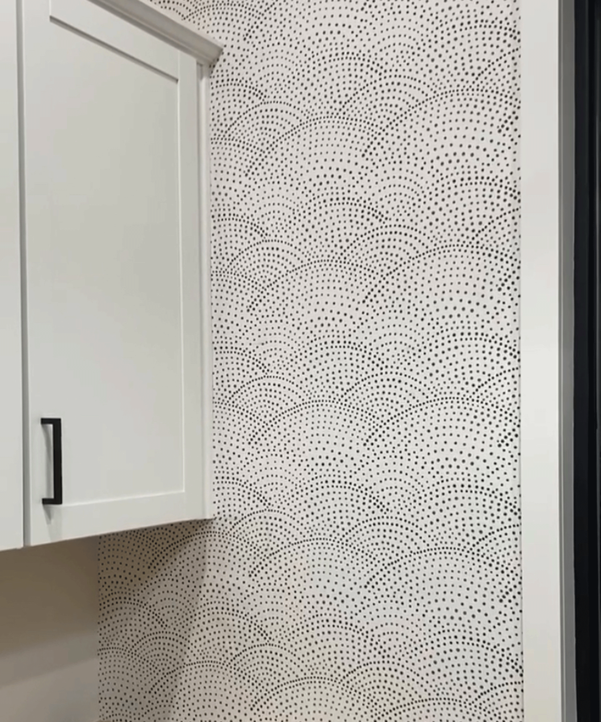 A close-up shot of white kitchen cupboards with handles, and monochrome spotted white and black wallpaper decor