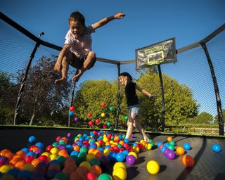 two kids jumping on a trampoline with balls and basketball hoop