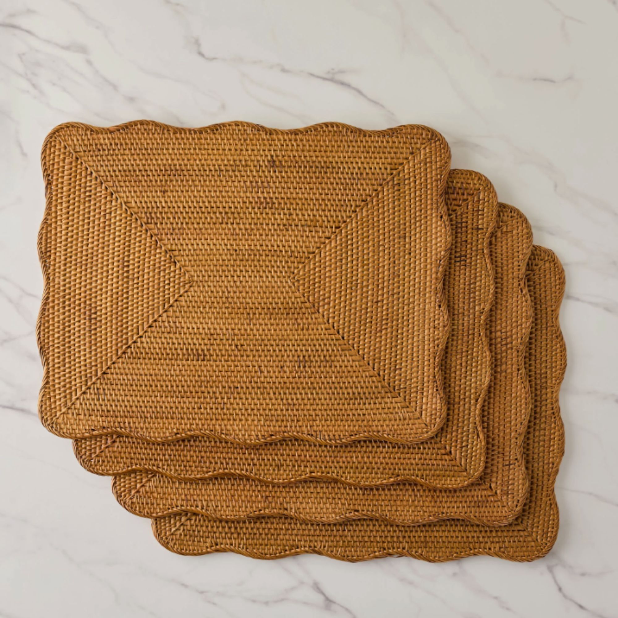 Set of four scallop edged rectangular rattan placemats on marble surface