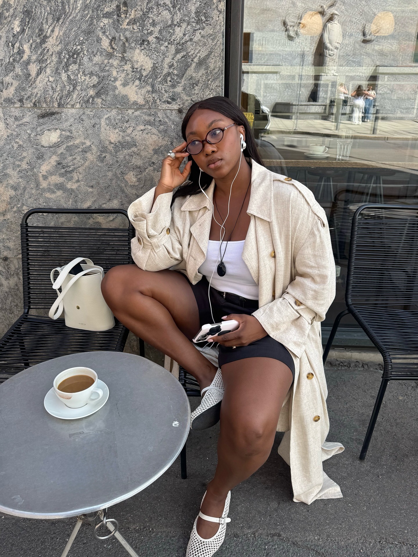 A woman sat outside a cafe with headphones in on her phone