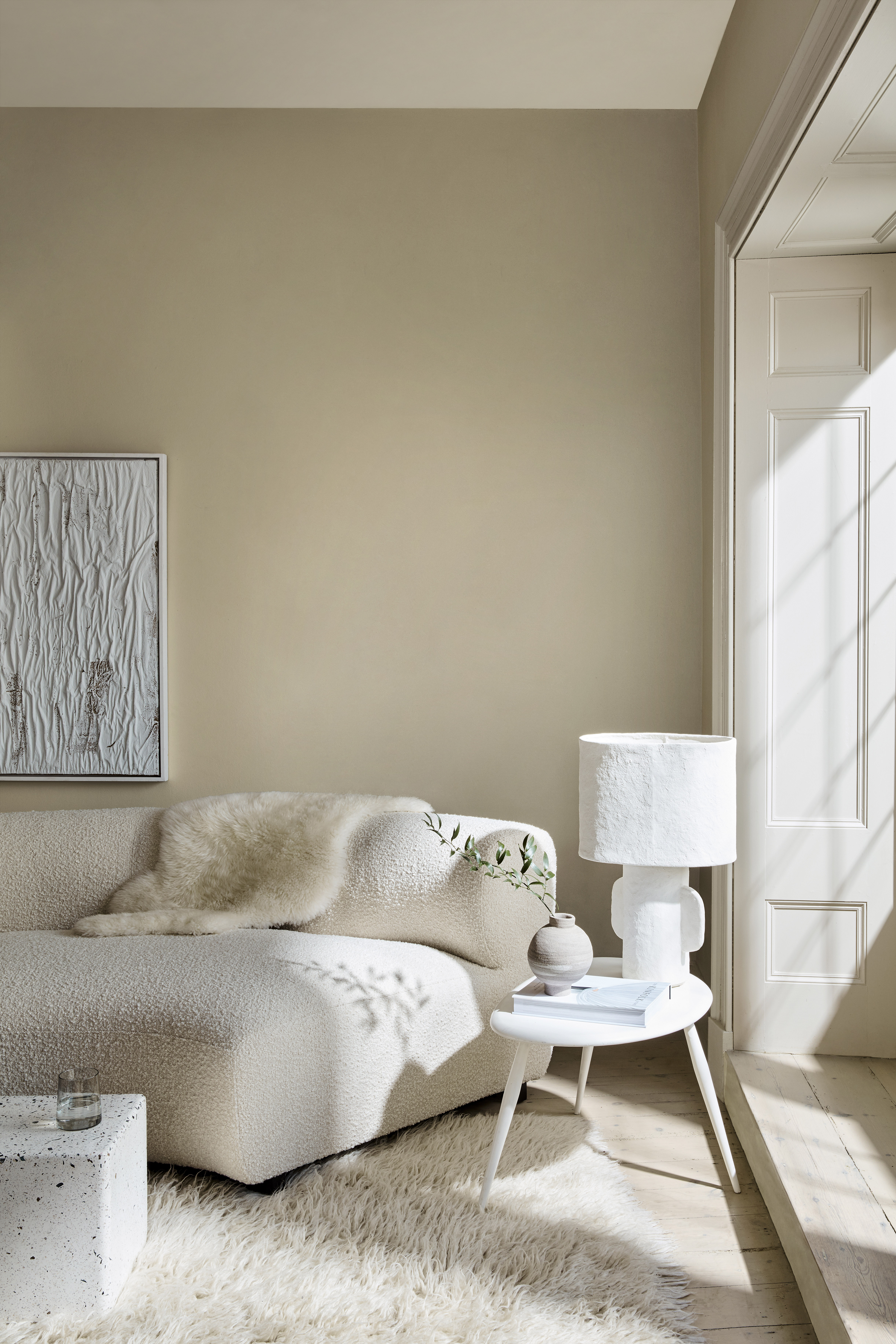 A fully cream and white small apartment living room, with sheepskin rug and throw and textured artwork.