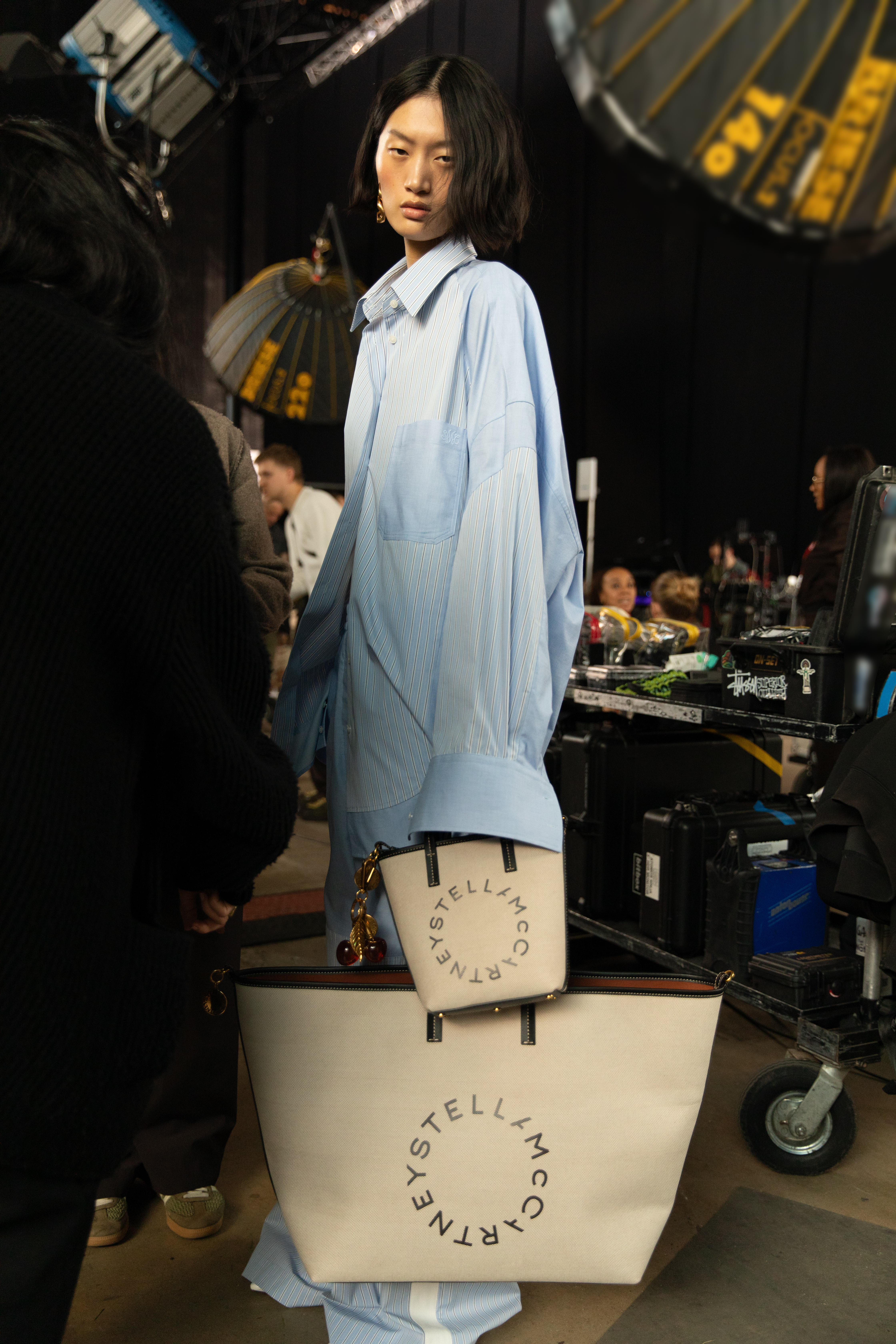 a model wearing a button up shirt and two tote bags from the stella mccartney collaboration