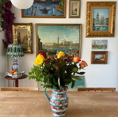 Vintage paintings in traditional frames in gallery wall behind wooden table holding vase of roses