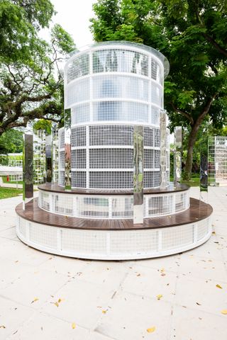A round multi leveled architectural structure in a park mad of wood and white square wire.