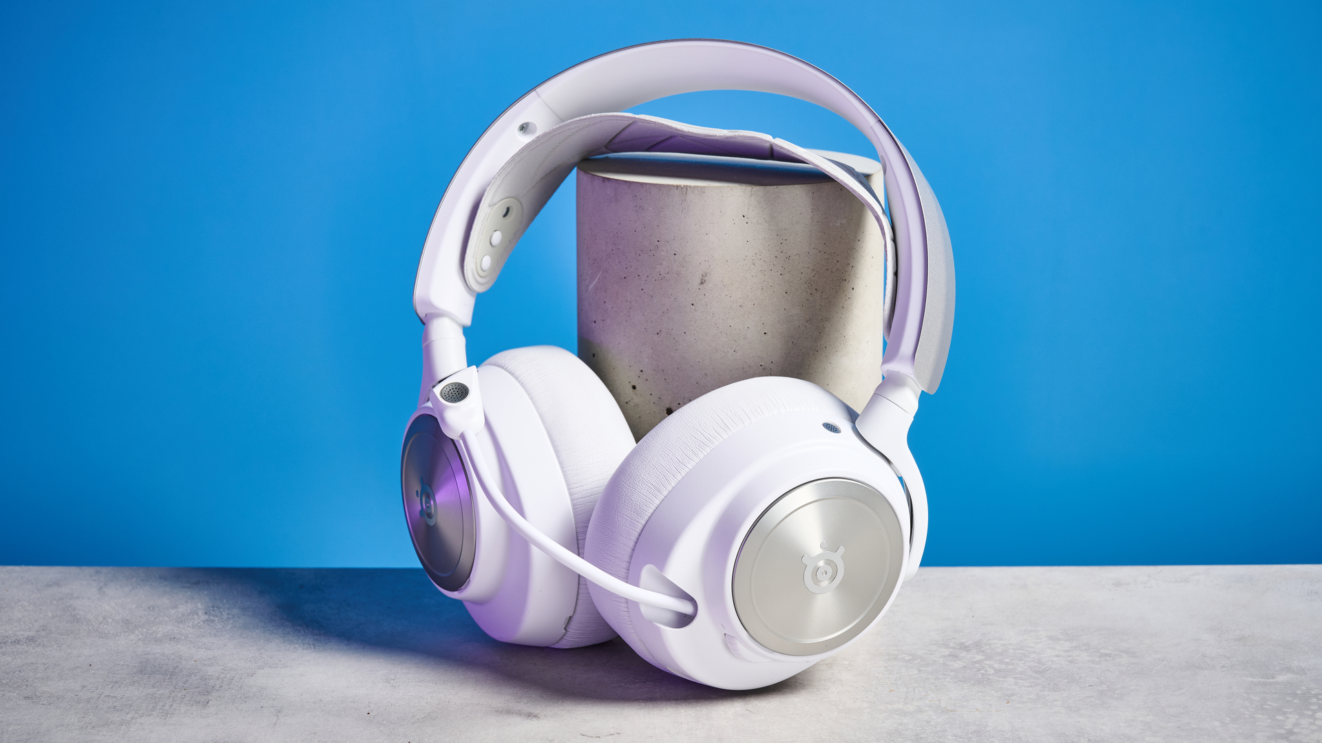 SteelSeries Arctis Nova Pro Wireless in white on a stone surface with a gentle purple reflection on the headset