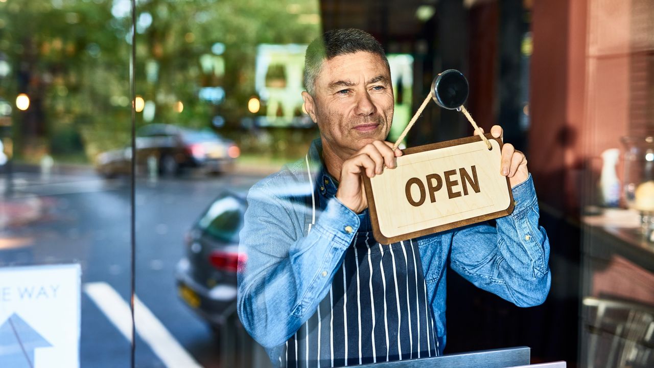 A business owner turns the sign in the window of his business over so it says Open.