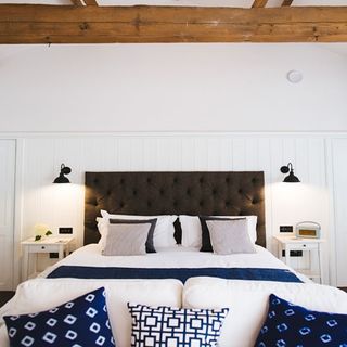 hotels bedroom with white wall grey headboard and white blue cushion