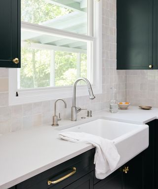 A kitchen with white soapstone worktops, green cabinets and a sink with silver metallic faucet