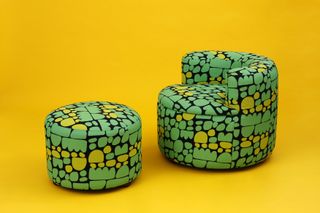 An armchair and footstool, both featuring round shapes, upholstered with a print designed by an aboriginal textile artist and featuring a black background with green and yellow motifs