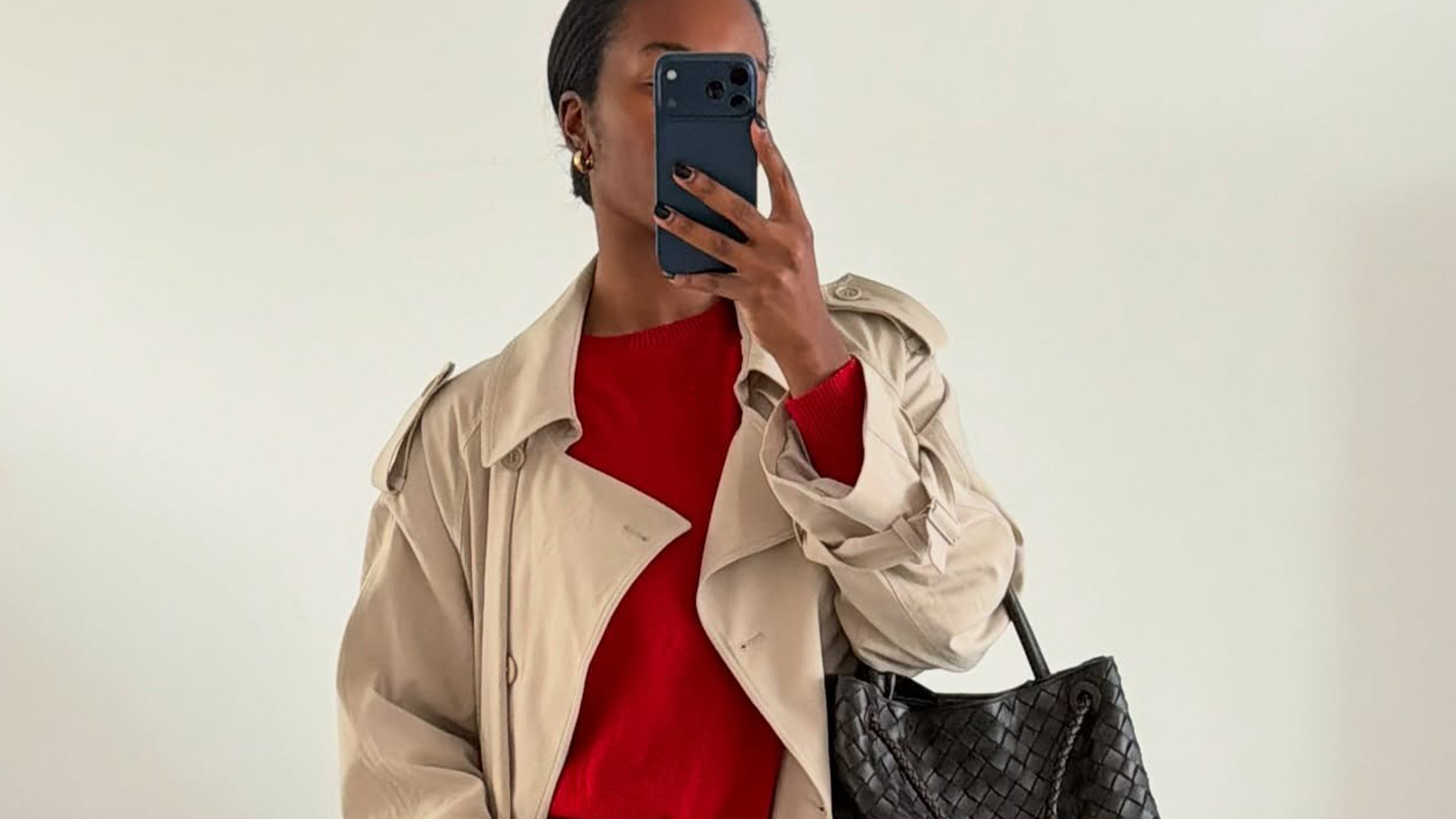 Woman wearing red t-shirt, trench coat, jeans, and brown Bottega Veneta Andiamo bag.