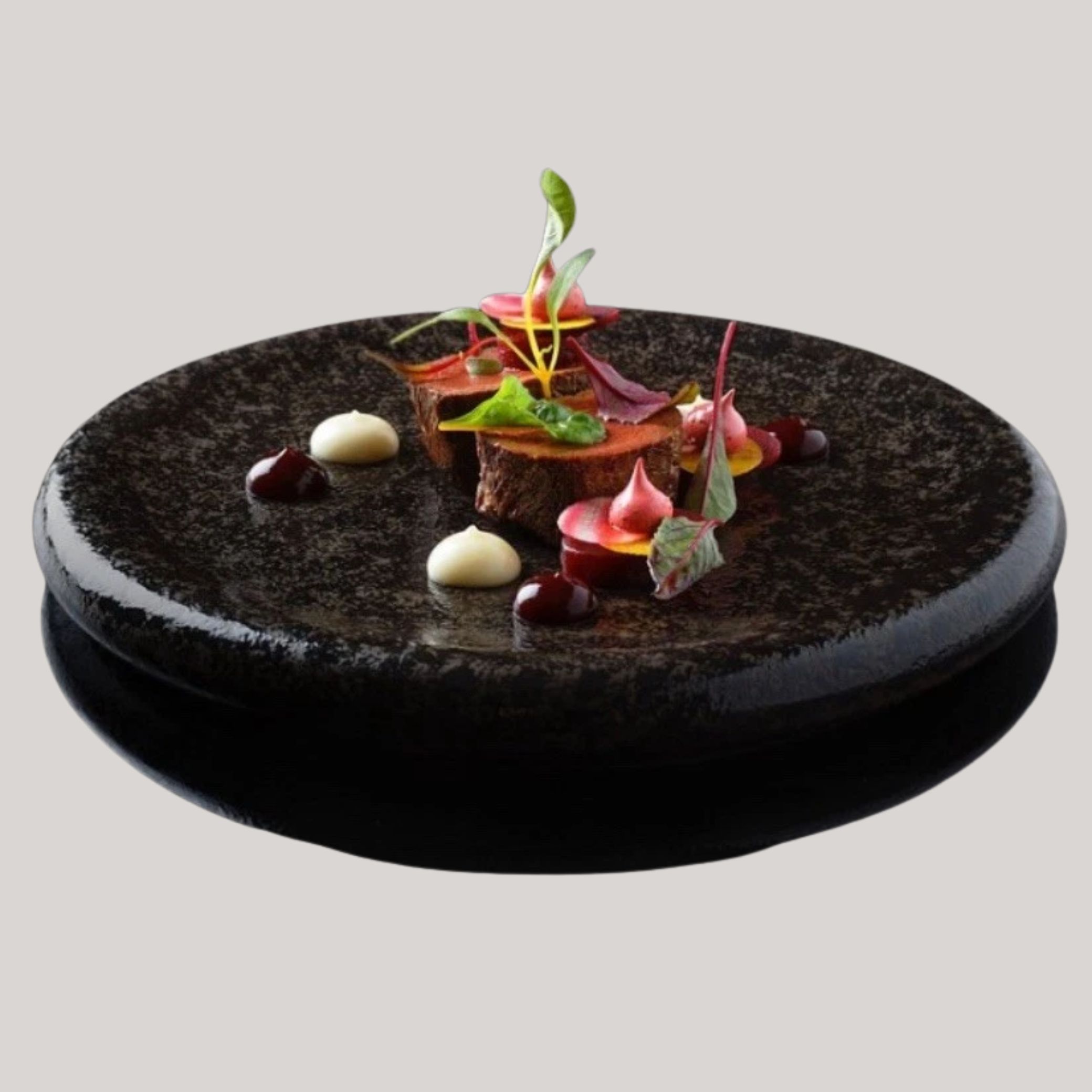 Studio Raw Black Satin Stone Plate filled with sculptural food, including colorful mousses, leafs, and crunchy layers, placed against a pale gray background.