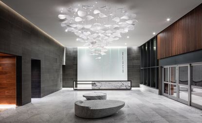 Brickell City Centre reception area with a reception counter, stone shaped chairs, dark grey marble walls, white marble floors and a large chandelier.