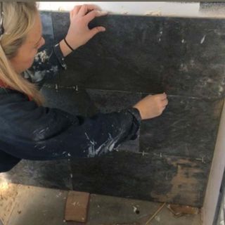 Blonde woman putting up the marble tiles against the wall