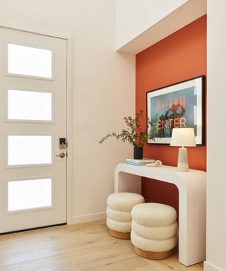 An entryway designed by Bobby Berk with a bright orange wall and a console table