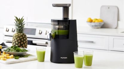 One of the best juicers, the Hurom H-AA slow juicer, making green juice in a white kitchen