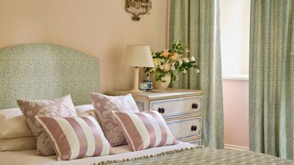 Tidy cream bedroom with soft greens bedding, headboard and curtains, with striped pink accent pillows and tiny floral prints