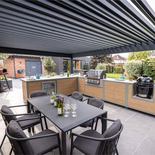 EO and Walker Landscape & Design covered outdoor kitchen area under pergola veranda with black table and chairs