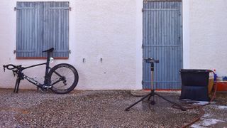 A S-Works Venge leans against a wall missing its front wheel, next to a workstand and bike-cleaning buckets