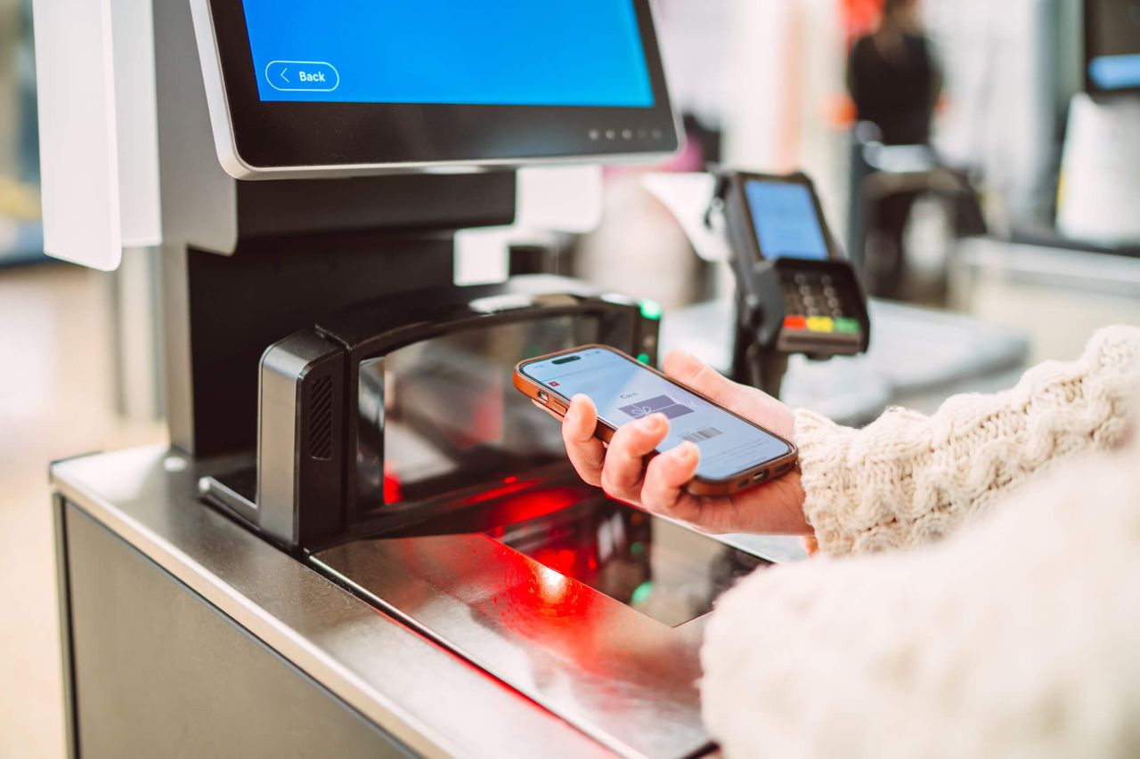 Close-up of a shopper using a smart phone to scan a digital barcode at a self-checkout terminal in a modern retail store