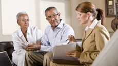 A financial adviser works with an older couple, who look very serious.