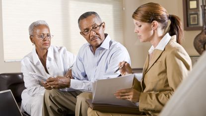 A financial adviser works with an older couple, who look very serious.