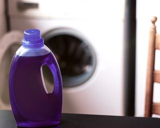 Close-up of purple laundry detergent concentrate in front of a wash machine