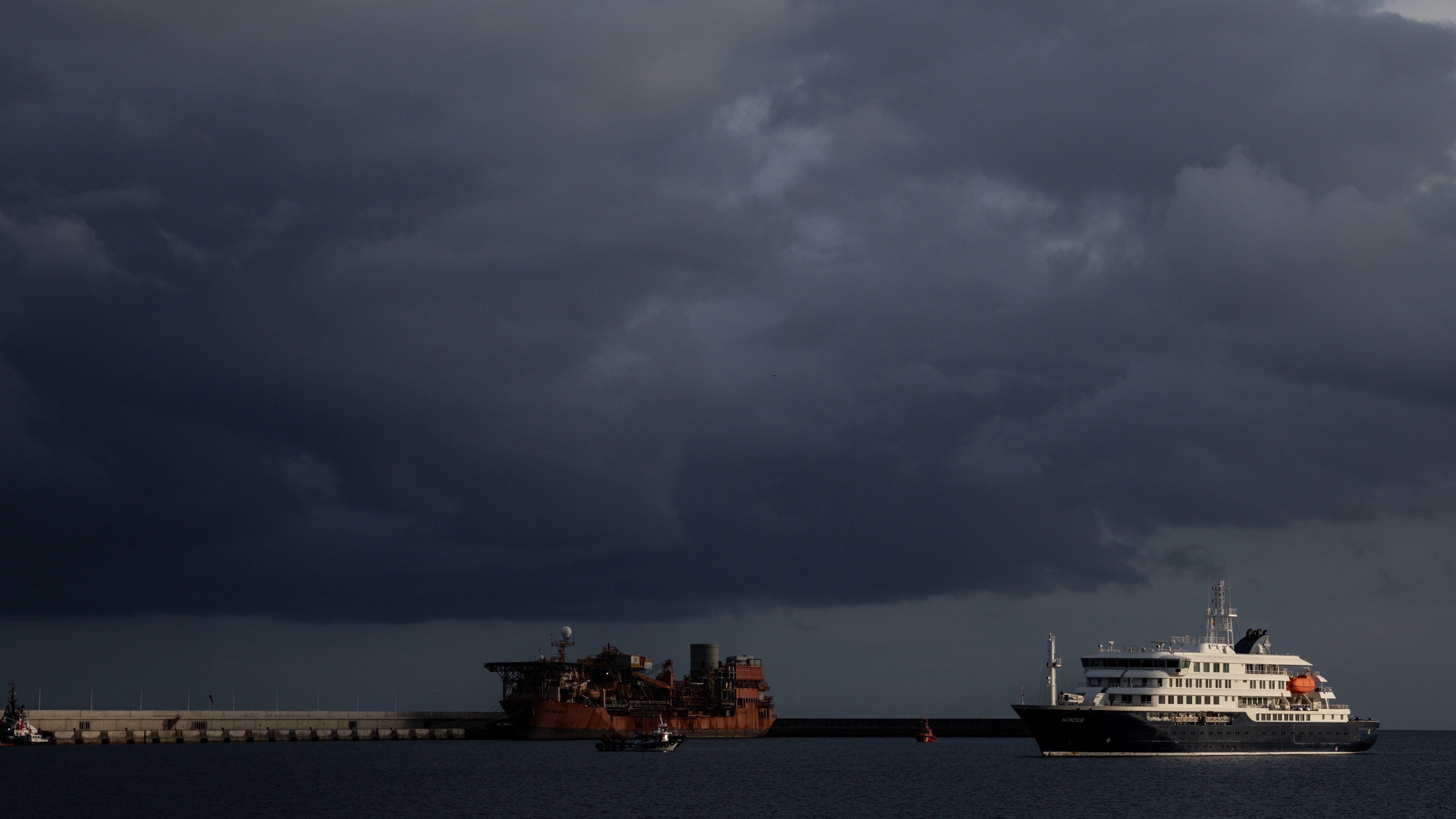 A cruise ship moves closer to a port as a storm cloud looms overhead.