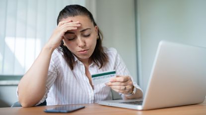 A woman stares at her credit card and looks worried.