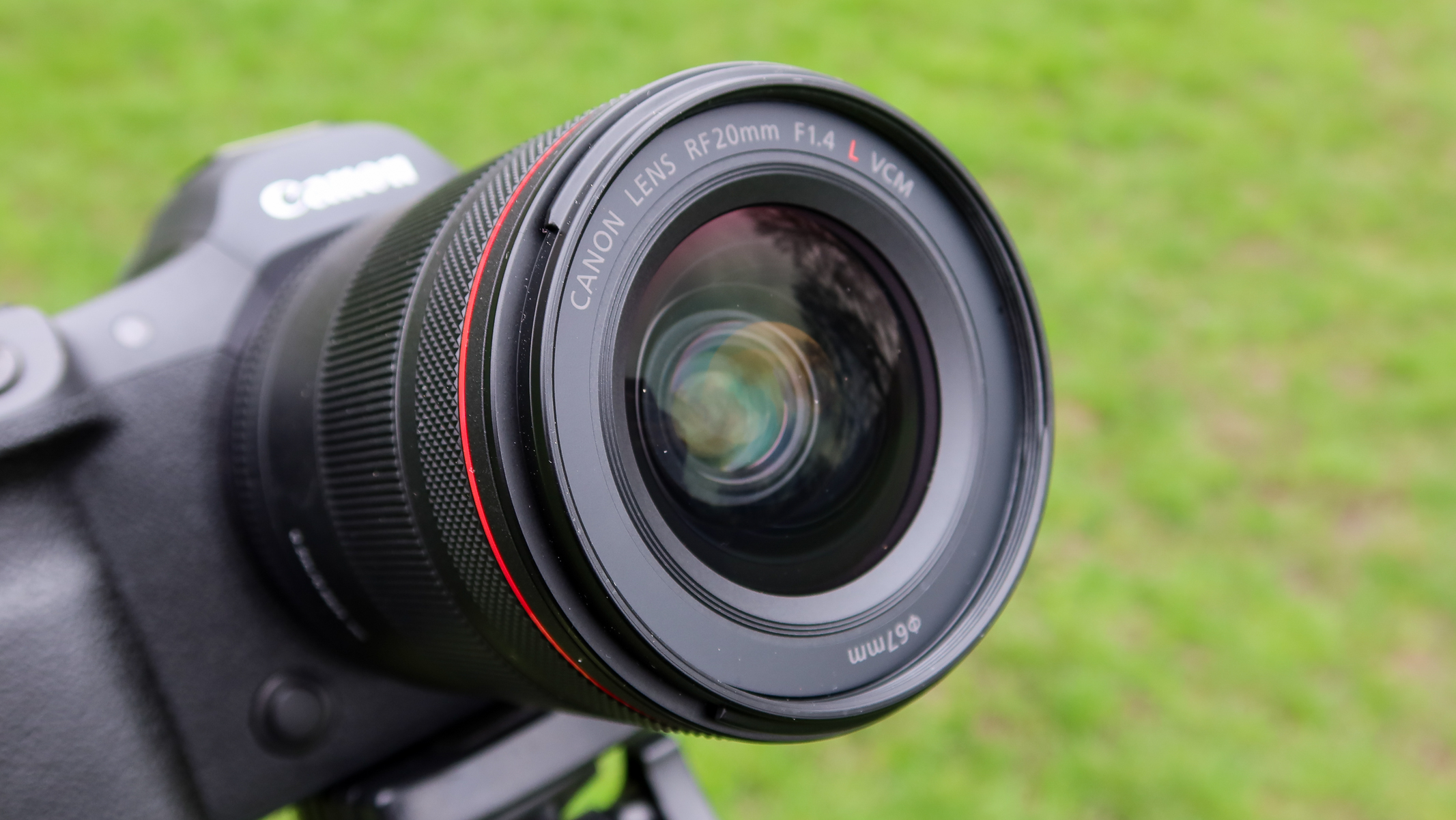 A close up of the Canon RF 20mm f/1.4 L VCM lens attached to the Canon EOS R5 II with grass in the background.