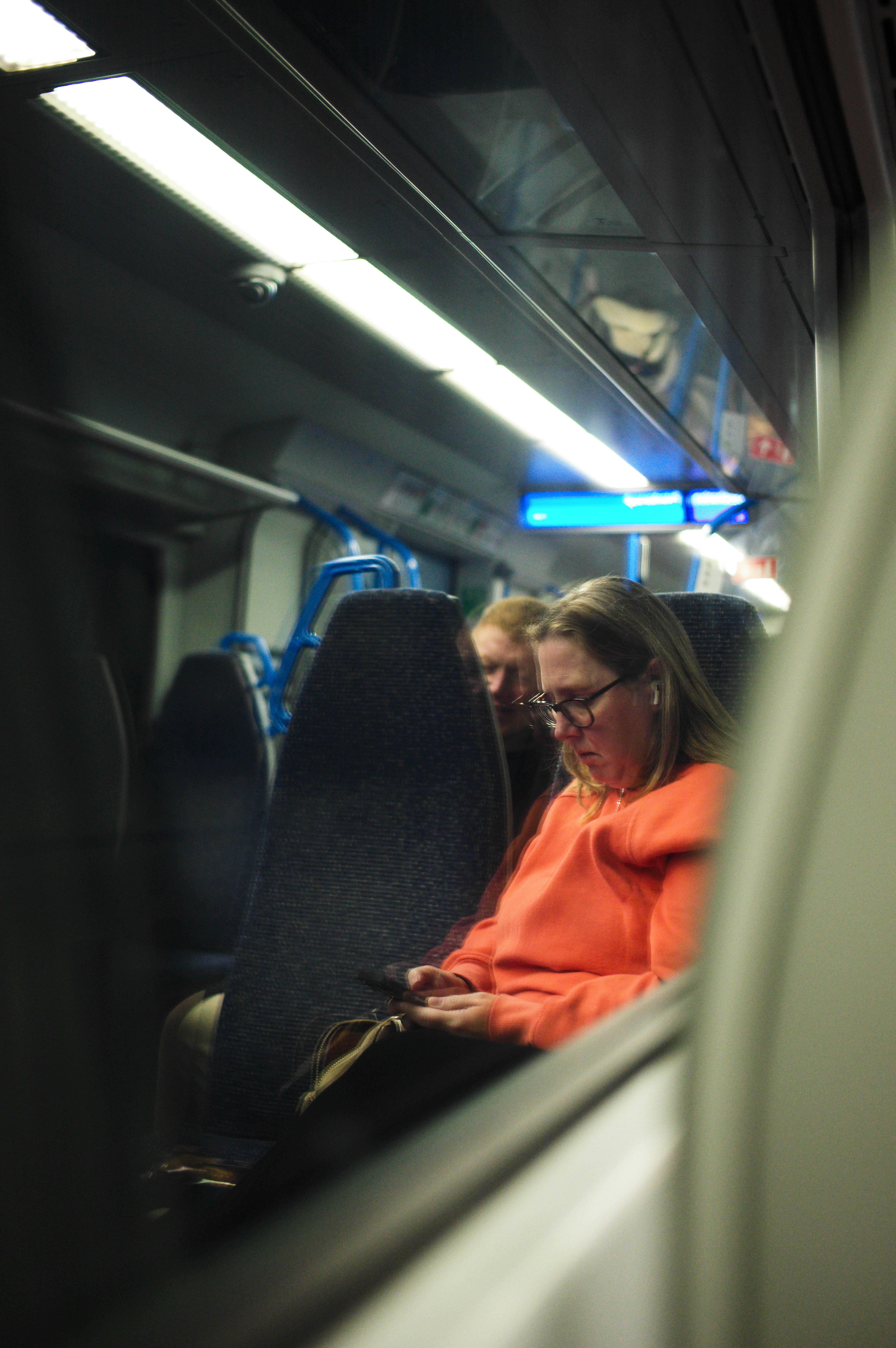 A person on their phone reflected in the window of a train