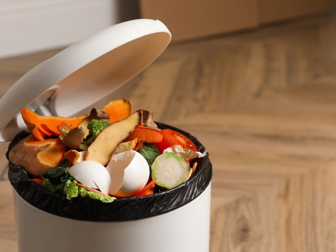 A small white trash can full to the brim with food waste