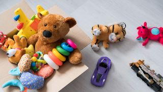 An array of toys, including teddy bears in a cardboard box on the floor