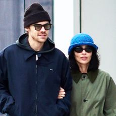 Zo&euml; Kravitz walking with Harry Styles in NYC while wearing an olive green coat, black pants, black sneakers, a The Row Ingrid bag, and blue crochet bucket hat