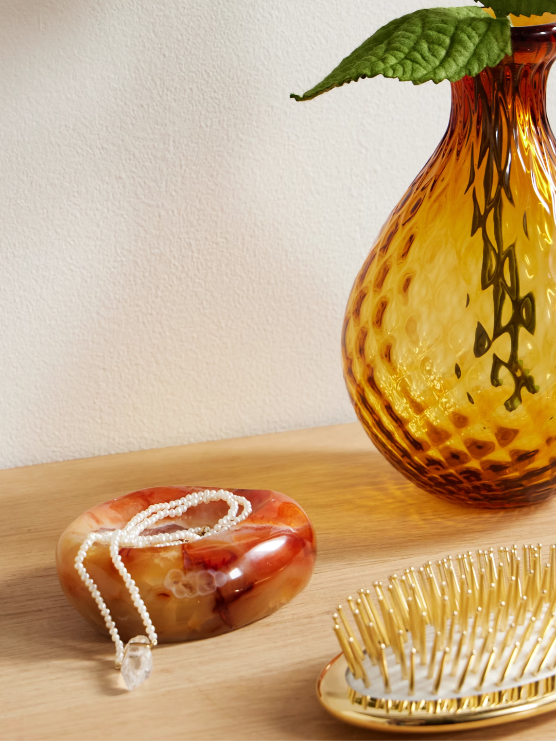 A small carnelian bowl by a gold hair brush and an ochre glass vase