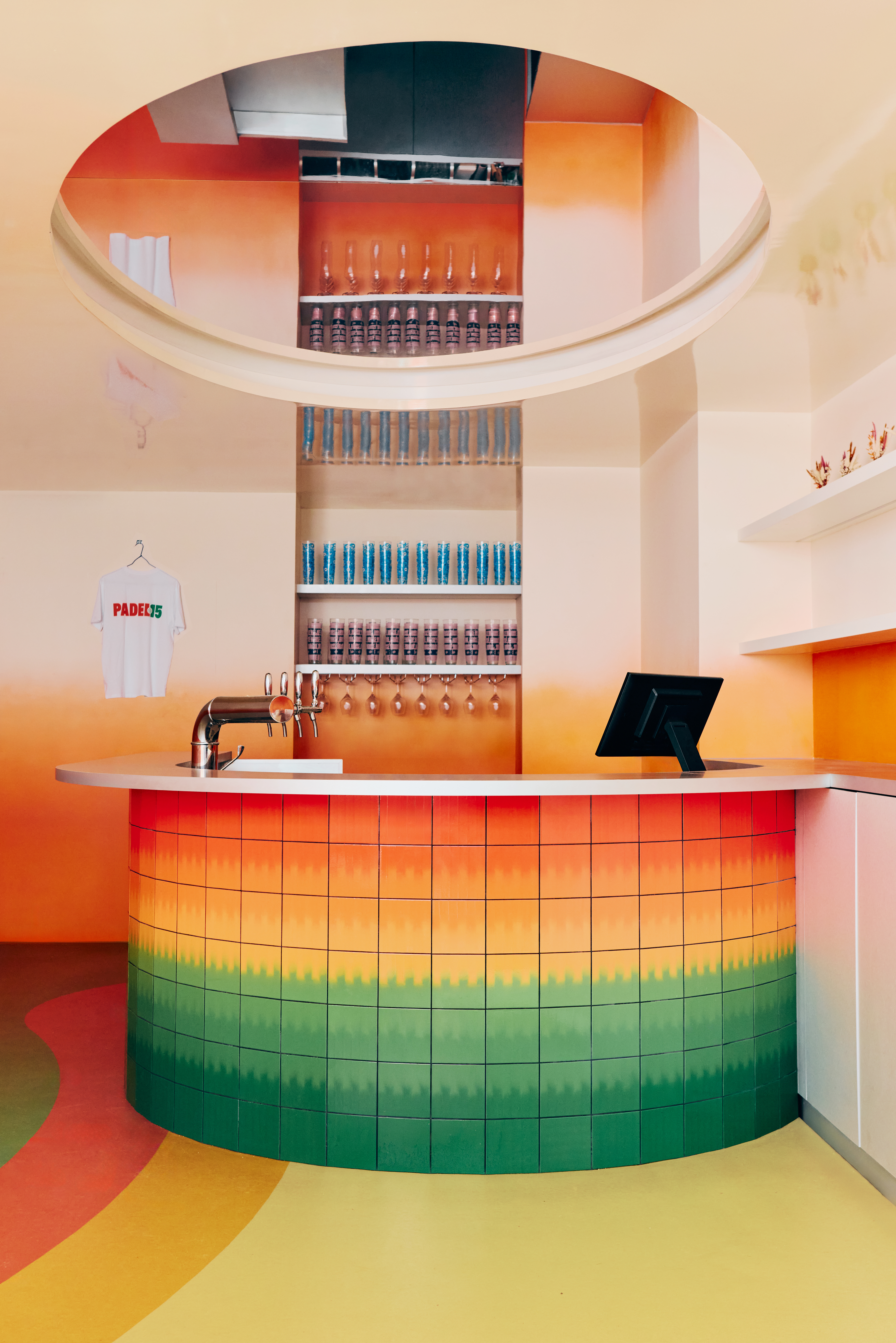 The restaurant and bar of a sports club features gradient green, orange, ochre, and yellow floors, walls, bar tiles, and furniture, each characterized by a whimsical essence.