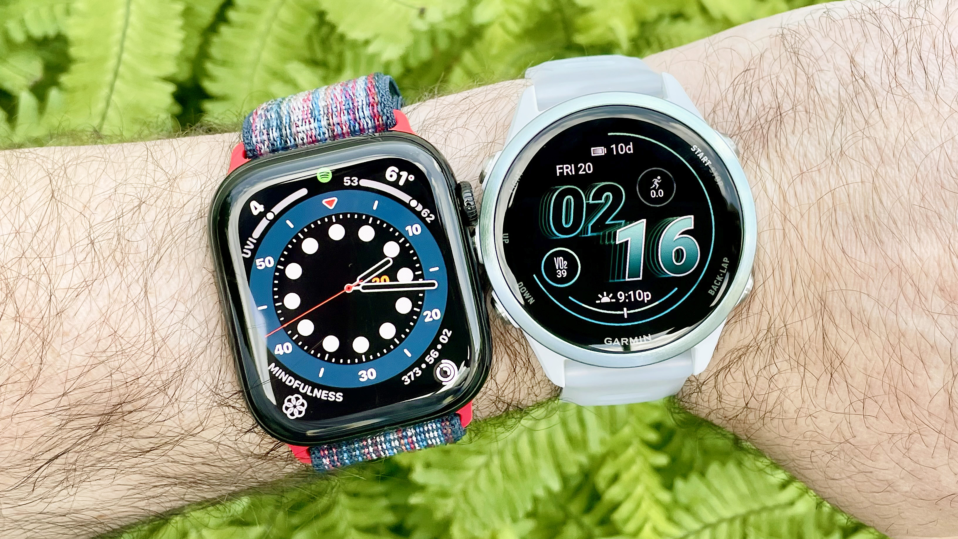 Apple Watch Series 10 next to a Garmin Forerunner 570 on a user's wrist with green foliage out of focus in the background