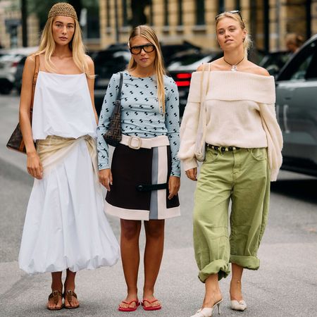 Three women pose for photos. The woman on the furthest left is wearing a white tank top and skirt set, then the middle is wearing a black skirt with a long-sleeve blue top, and on the right, she's wearing a white sweater and green oversized pants.
