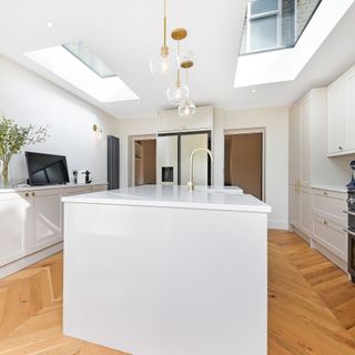 white kitchen in side return extension with wooden herringbone flooring and large kitchen island