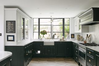 A dark green U shaped kitchen looking out onto a garden