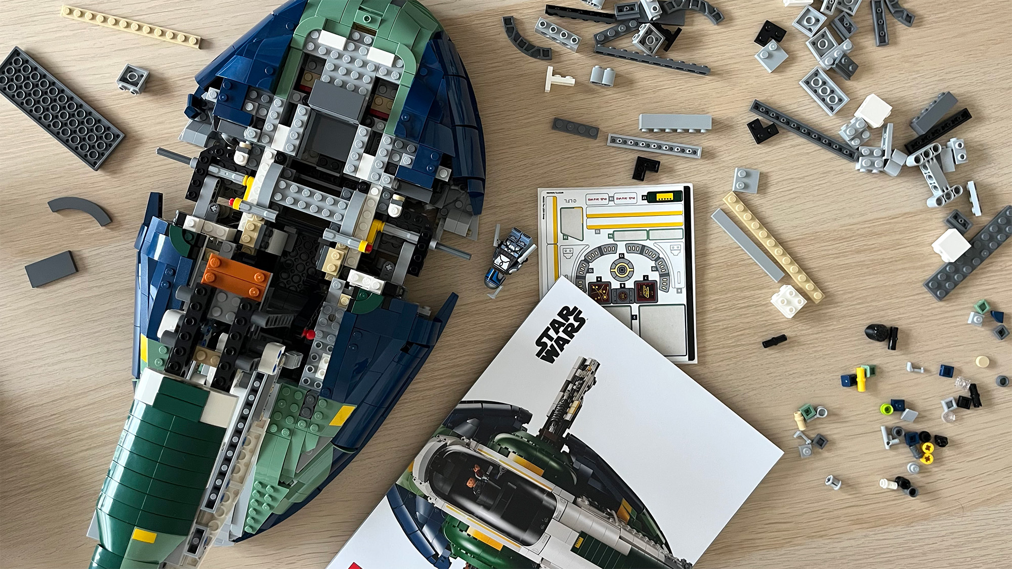 Lego Star Wars UCS Jango Fett&rsquo;s Firespray-Class Starship (75409) mid-build on wooden tabletop next to lots of Lego pieces and an instruction booklet 