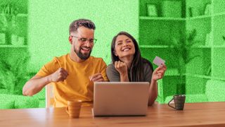 Young couple looking happy, sitting at a table in front of a laptop.