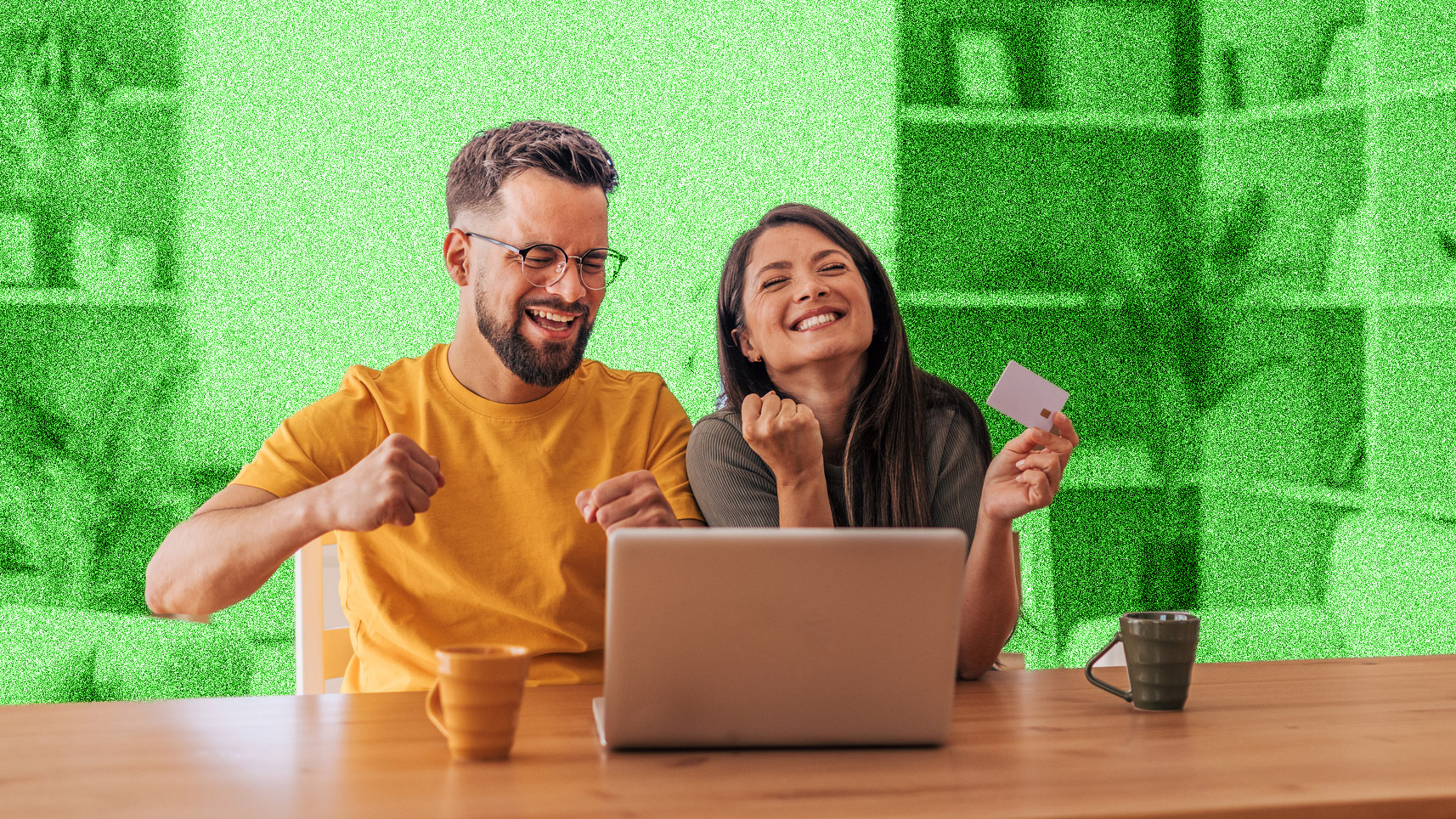 Young couple looking happy, sitting at a table in front of a laptop.