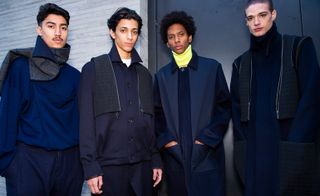 Four male models wearing clothing by Chalayan in shades on blue.