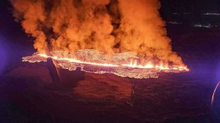 lava spewing from a fissure as seen from above at night with lava flowing across the ground